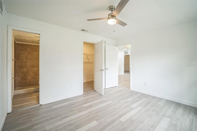 unfurnished bedroom with a closet, a walk in closet, light hardwood / wood-style floors, ceiling fan, and ensuite bathroom