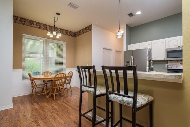 kitchen with stainless steel appliances, white cabinetry, a kitchen bar, dark hardwood / wood-style floors, and decorative light fixtures