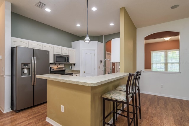 kitchen with hanging light fixtures, wood-type flooring, white cabinetry, and appliances with stainless steel finishes