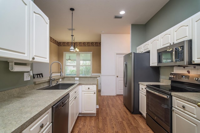 kitchen with stainless steel appliances, white cabinetry, decorative light fixtures, sink, and dark wood-type flooring