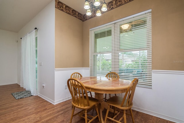 dining area with hardwood / wood-style floors, lofted ceiling, and a notable chandelier