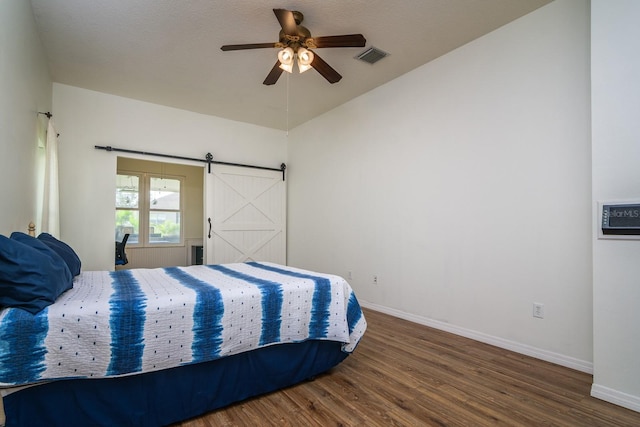 bedroom with a textured ceiling, a barn door, ceiling fan, and dark hardwood / wood-style floors