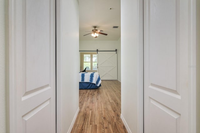 hall with a barn door and wood-type flooring