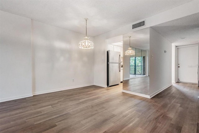 empty room featuring hardwood / wood-style flooring, a chandelier, and a textured ceiling