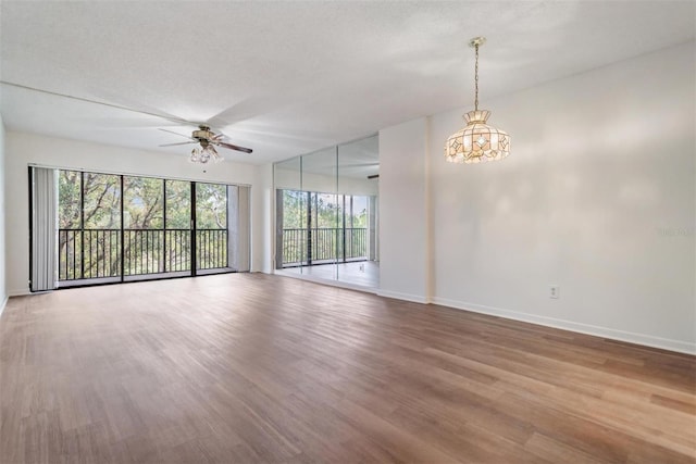 empty room with hardwood / wood-style floors, a wealth of natural light, ceiling fan with notable chandelier, and a textured ceiling