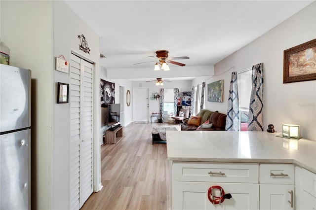 kitchen featuring stainless steel fridge, white cabinets, light hardwood / wood-style floors, and ceiling fan