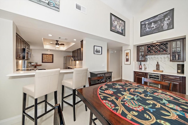 dining space with ceiling fan, beverage cooler, a raised ceiling, and bar