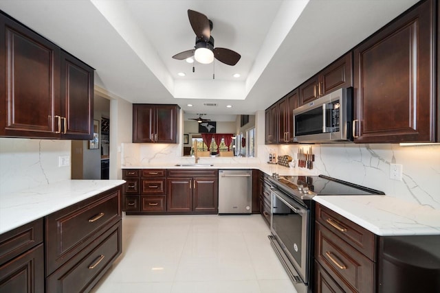 kitchen featuring ceiling fan, sink, a tray ceiling, decorative backsplash, and appliances with stainless steel finishes