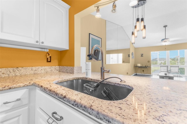 kitchen with light stone counters, sink, white cabinets, and decorative light fixtures