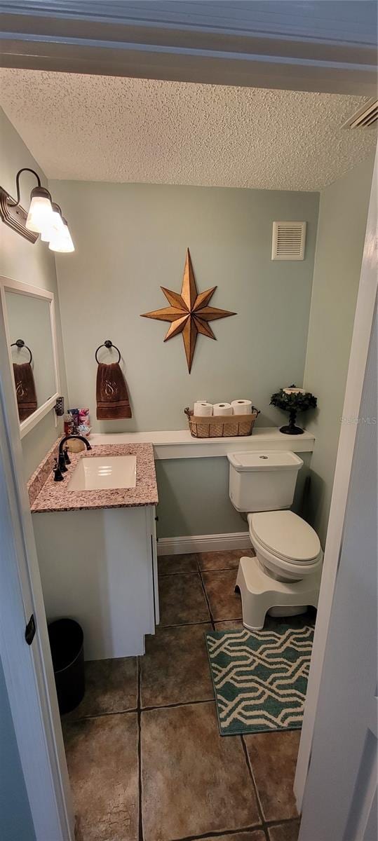 bathroom featuring vanity, tile patterned floors, a textured ceiling, and toilet