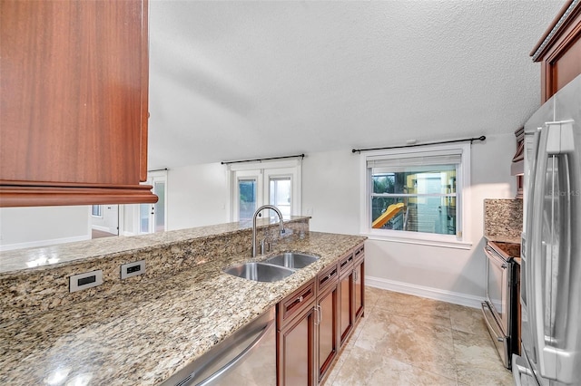 kitchen featuring a textured ceiling, sink, light stone counters, and stainless steel appliances