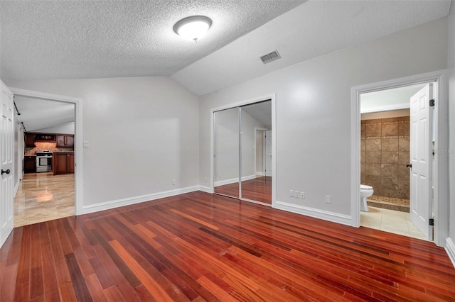 unfurnished bedroom featuring a closet, vaulted ceiling, hardwood / wood-style flooring, and a textured ceiling