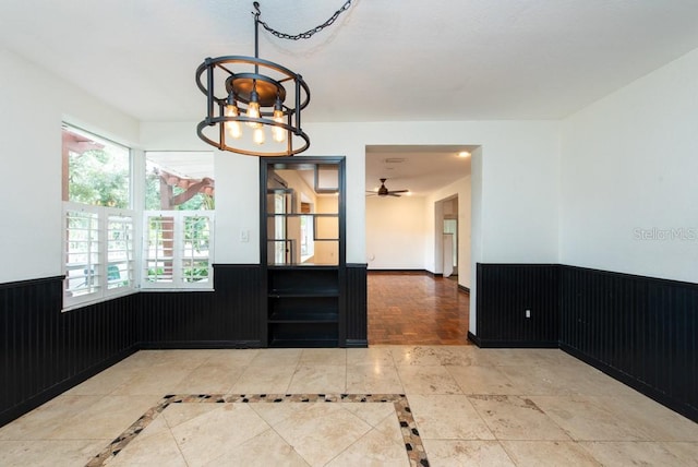 unfurnished dining area featuring wood walls, a wealth of natural light, and ceiling fan with notable chandelier