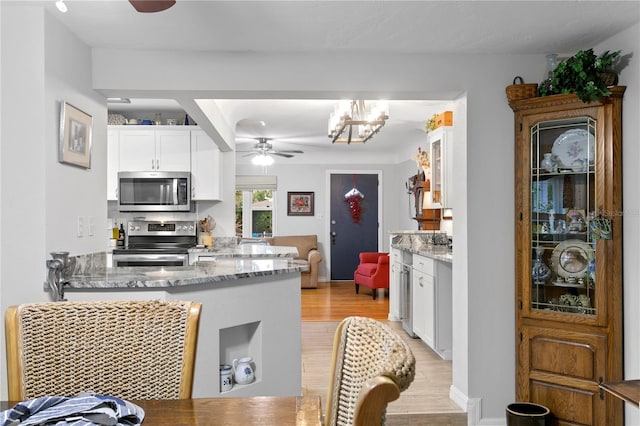 kitchen featuring light stone counters, appliances with stainless steel finishes, kitchen peninsula, ceiling fan, and white cabinets