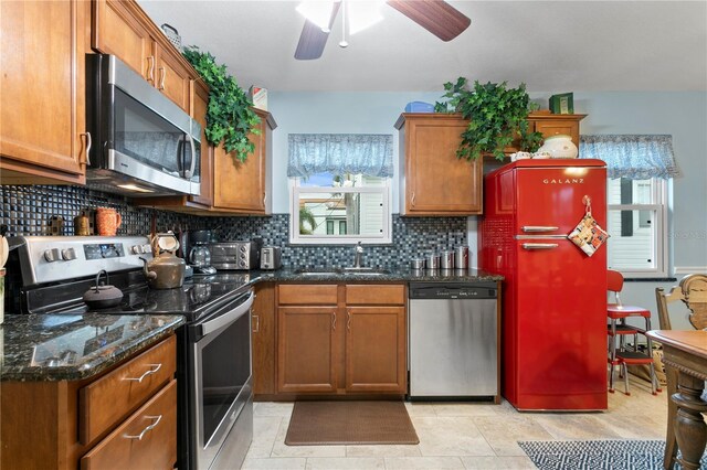 kitchen with sink, dark stone counters, light tile patterned floors, ceiling fan, and stainless steel appliances