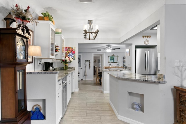 kitchen featuring white cabinetry, stainless steel fridge, kitchen peninsula, and light stone counters