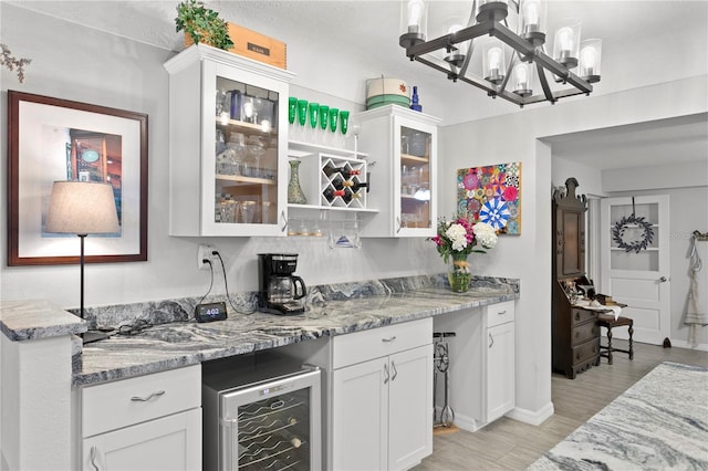 kitchen with decorative light fixtures, white cabinets, beverage cooler, light stone countertops, and light hardwood / wood-style flooring