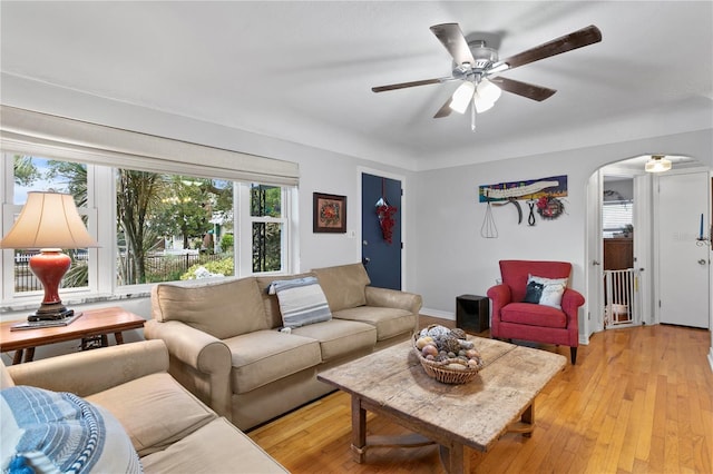 living room with a ceiling fan, arched walkways, and light wood finished floors