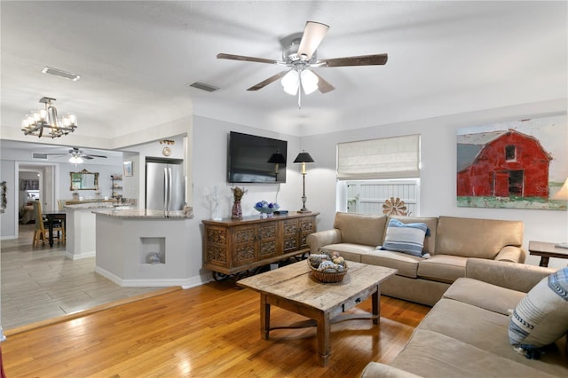 living area featuring visible vents, light wood-style flooring, baseboards, and ceiling fan with notable chandelier