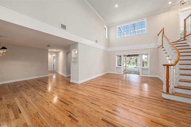 unfurnished living room with a towering ceiling, light hardwood / wood-style floors, and ornamental molding