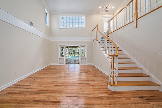 unfurnished living room with crown molding, a towering ceiling, a chandelier, and light wood-type flooring