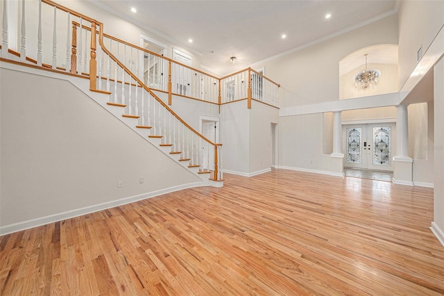 unfurnished living room featuring light wood-type flooring, ornamental molding, a towering ceiling, and a chandelier