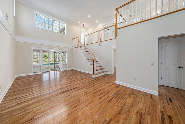 unfurnished living room featuring crown molding, a towering ceiling, and light hardwood / wood-style floors