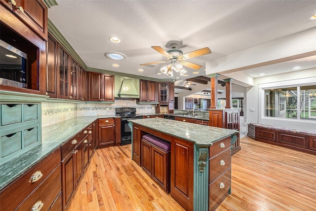 kitchen featuring a center island, decorative columns, light hardwood / wood-style floors, black appliances, and custom range hood