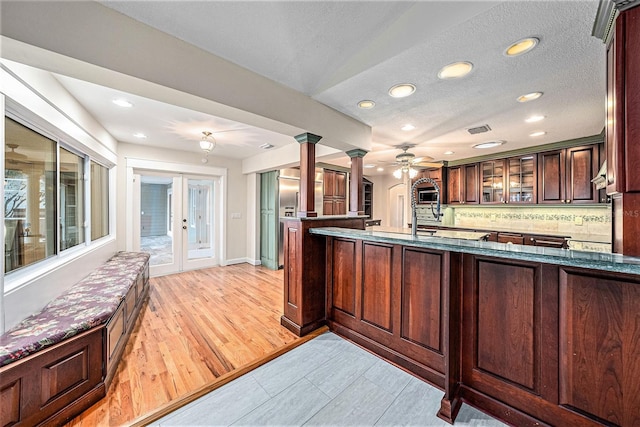 kitchen featuring backsplash, ornate columns, kitchen peninsula, and light hardwood / wood-style floors