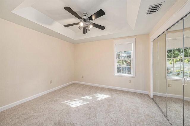 unfurnished bedroom featuring a raised ceiling, ceiling fan, a closet, and carpet