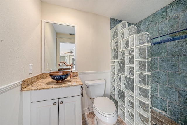 bathroom with a tile shower, ceiling fan, a textured ceiling, toilet, and vanity