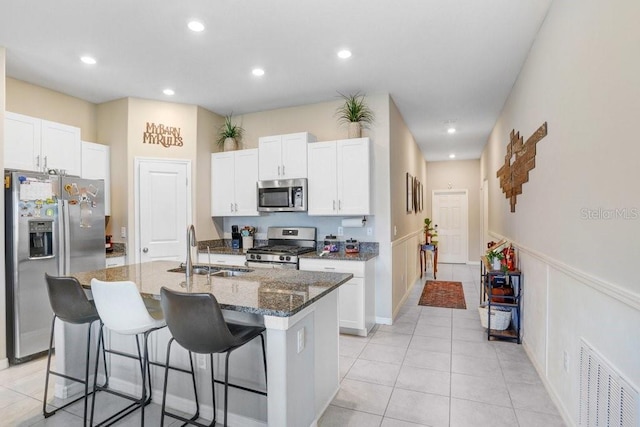 kitchen featuring a center island with sink, dark stone counters, appliances with stainless steel finishes, sink, and white cabinets