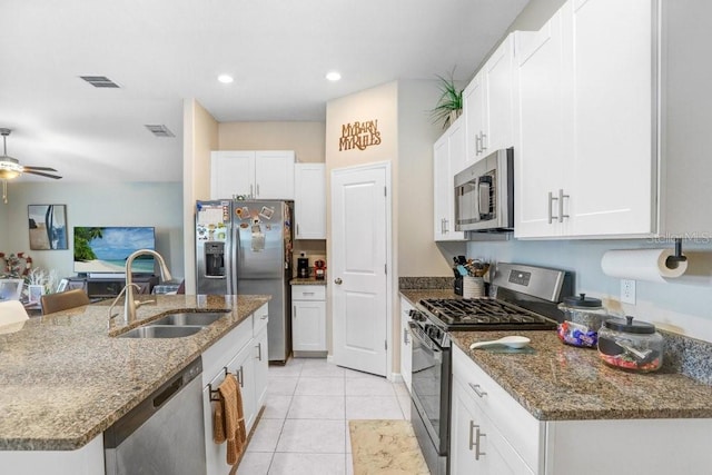 kitchen with stainless steel appliances, sink, dark stone countertops, an island with sink, and white cabinets