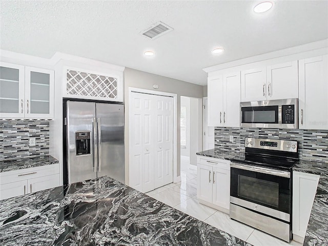 kitchen with dark stone counters, white cabinetry, appliances with stainless steel finishes, a textured ceiling, and decorative backsplash