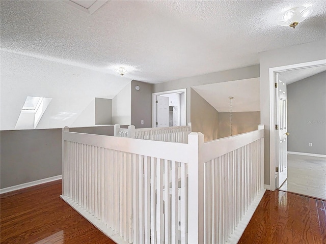 hallway with vaulted ceiling with skylight, hardwood / wood-style floors, and a textured ceiling