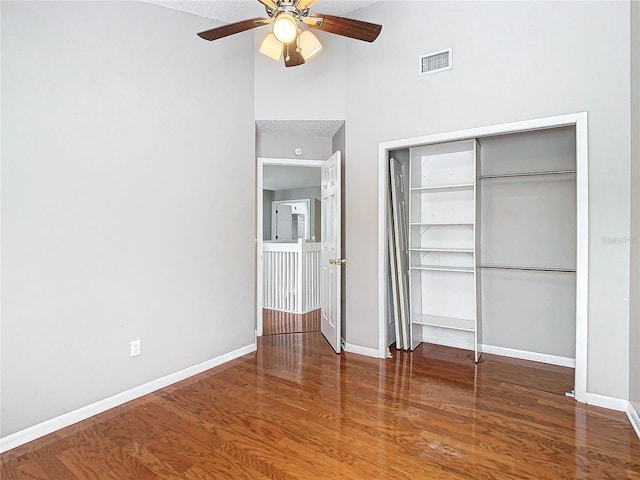 unfurnished bedroom featuring hardwood / wood-style flooring, a towering ceiling, ceiling fan, and a closet