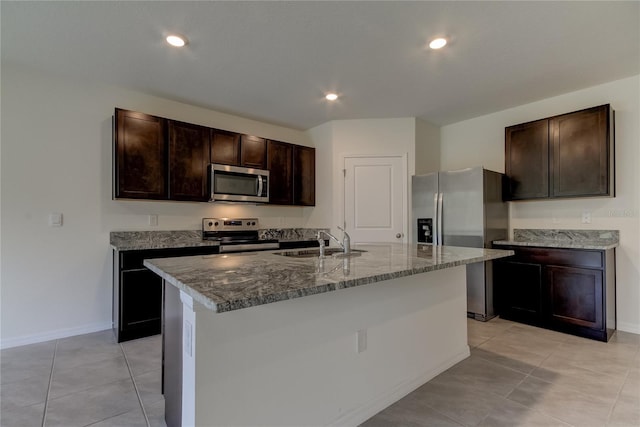 33351 Apricot Tree Ct, Wesley Chapel, FL 33543 - kitchen featuring stainless steel appliances, dark stone counters, dark brown cabinetry, a kitchen island with sink, and light tile patterned floors