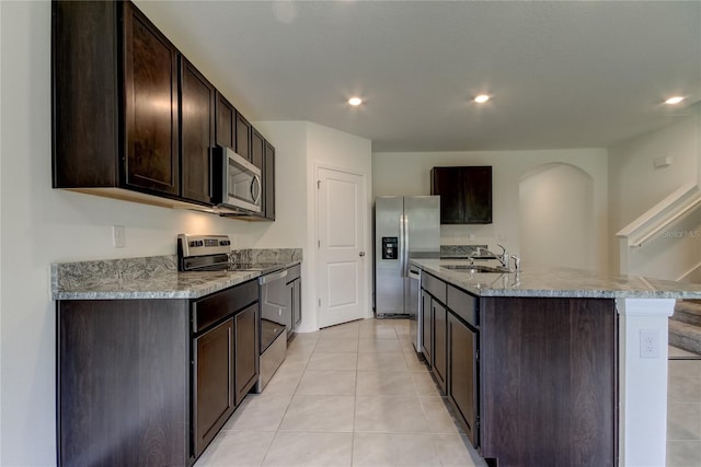 33351 Apricot Tree Ct, Wesley Chapel, FL 33543 - kitchen featuring appliances with stainless steel finishes, dark brown cabinets, a center island with sink, arched walkways, and light tile patterned flooring