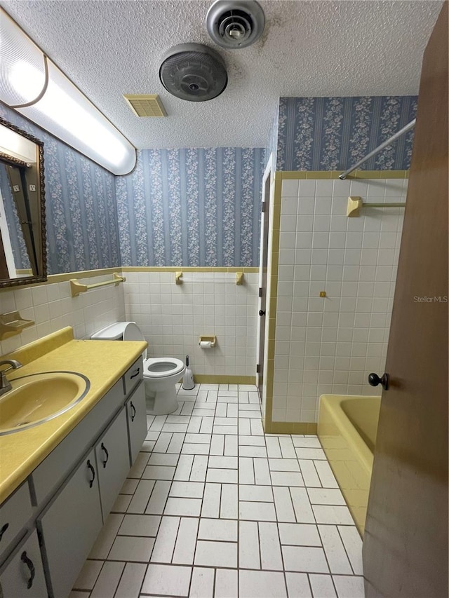 full bathroom featuring tile patterned flooring, a textured ceiling, toilet, and tile walls