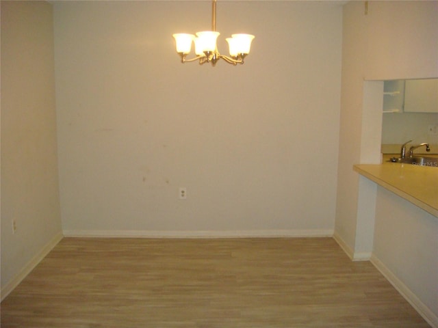 unfurnished dining area featuring an inviting chandelier, sink, and light hardwood / wood-style flooring