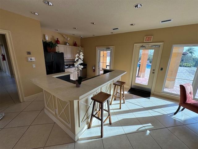 kitchen featuring black refrigerator with ice dispenser, light tile patterned flooring, tile counters, a kitchen breakfast bar, and a center island