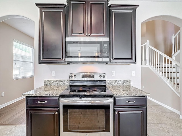 kitchen with light stone countertops, dark brown cabinets, light tile patterned floors, and stainless steel appliances