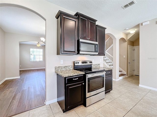 kitchen with stainless steel appliances, light stone counters, ceiling fan, a textured ceiling, and light hardwood / wood-style flooring