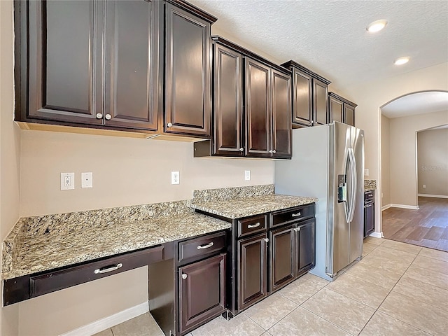 kitchen featuring dark brown cabinetry, stainless steel refrigerator with ice dispenser, light hardwood / wood-style flooring, and light stone counters