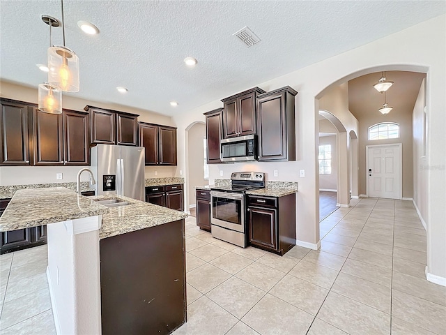 kitchen featuring appliances with stainless steel finishes, a textured ceiling, dark brown cabinetry, hanging light fixtures, and sink