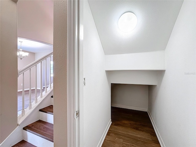 staircase featuring wood-type flooring, lofted ceiling, and an inviting chandelier