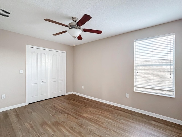 unfurnished bedroom with hardwood / wood-style flooring, a textured ceiling, ceiling fan, and a closet