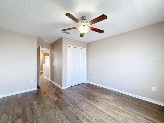 unfurnished bedroom with ceiling fan, a textured ceiling, a closet, and dark hardwood / wood-style flooring