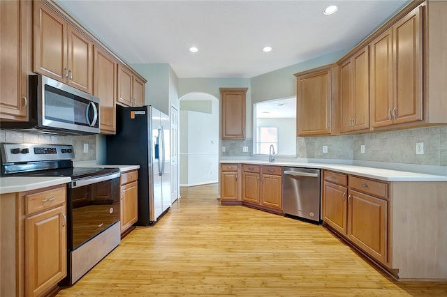 kitchen featuring backsplash, sink, light wood-type flooring, and appliances with stainless steel finishes