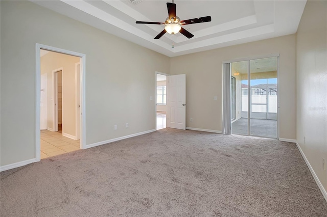 unfurnished room with ceiling fan, a wealth of natural light, light colored carpet, and a raised ceiling